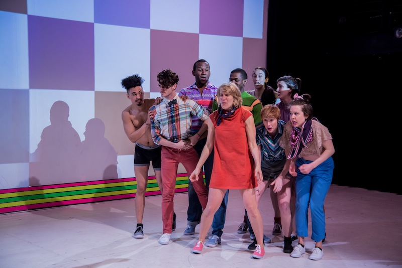 Dancers in colorful street clothes huddle in a group and make funny faces